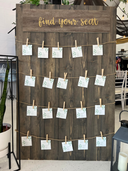 A large barnwood seating chart with seating assignments displayed using clothespins on a rope, mounted on a wooden board with the text 'find your seat' at the top.