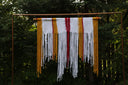 A bohemian style macrame hanging with white, gold, red, and purple threads arranged in a decorative pattern.