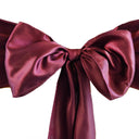 A close-up image of a burgundy satin chair sash with a bow shape.