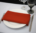 Brunt Orange napkin on a white plate with silverware and glasses on a white table