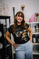 Woman wearing a black t-shirt with a graphic design in a room with shelves and decorative items.