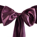 A close-up image of an eggplant purple satin chair sash with a bow tie shape.