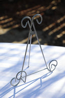 A silver tabletop easel with a triangular base and ornate curved supports for displaying artwork.