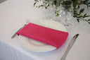 A fuchsia colored polyester napkin on a plate, with a white tablecloth and cutlery visible in the background.