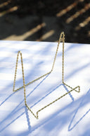 A gold wire tabletop easel standing on a shadowy surface, possibly a table.