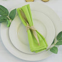 A lime green polyester napkin tied with a burlap ribbon, presented on a white plate with a burlap decoration and green leaves around it.