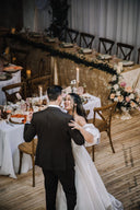 Wedding couple dancing in a decorated banquet hall with tables and floral arrangements.