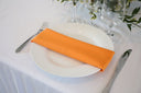 An orange polyester napkin is placed on a white plate on a table, with a fork on the left side and a knife on the right side of the plate.