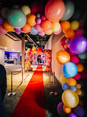 Colorful balloon archway at an event entrance with a red carpet.