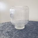 A ribbed Glass Barrel Vase sitting on a blue velvet tablecloth with white background