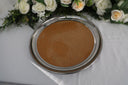 A round metal serving platter with a cork surface, placed on a white tablecloth, with a bouquet of flowers arranged at the top of the frame.