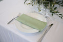 A sage green polyester napkin is placed on a white plate, set on a table with cutlery and a white tablecloth.
