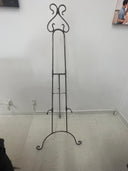 A silver iron easel standing on a white floor against a wall, with no canvas attached.