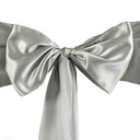 A close-up of a silver satin chair sash with a bow tie in the center.