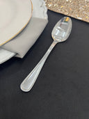 A silver spoon placed on a black surface with a plate and napkin in the background.