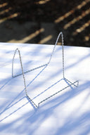 A silver tabletop easel placed on a table, with the easel's shadow cast on the table's surface.