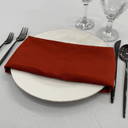 Set table with a white plate, terracotta  napkin, black cutlery, and clear glasses on a light gray surface.