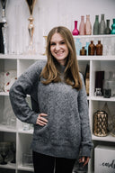Woman wearing a gray sweater standing in front of a shelf with decorative items