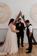 Wedding ceremony with a couple and an officiant in front of decorative wall art.