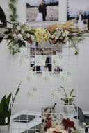 A white photo display grate with square frames arranged in a grid pattern, adorned with floral arrangements and decorative items.