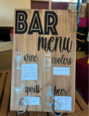 A wooden bar menu chart with handwritten entries for wine, spirits, beer, and coolers categories.