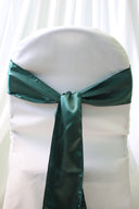 A hunter green satin chair sash tied in a bow on a white chair cover, providing a contrast in colors.