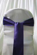 A purple satin chair sash tied in a bow on a white chair cover, with a focus on the sash.