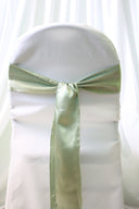 A sage satin chair sash tied in a bow on a white chair cover.
