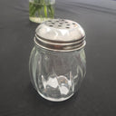 Clear glass spice shaker with silver top on a dark background